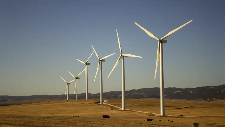 Uma paisagem bonita do Uruguai mostrando turbinas eólicas girando ao fundo, com campos verdes ou gado pastando na frente, simbolizando a harmonia entre tecnologia e natureza.