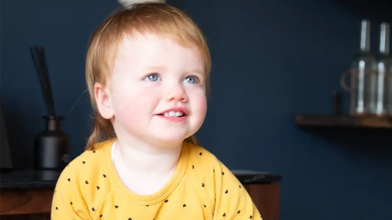 A pequena Opal Sandy sorrindo durante exames médicos, após recuperar a audição graças a um tratamento genético inovador.