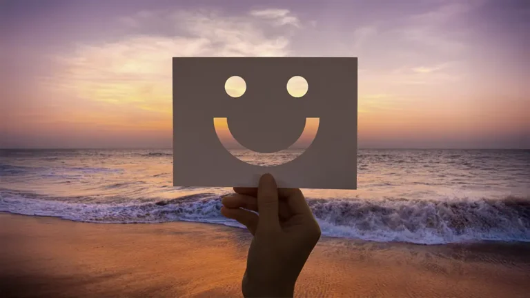 Mão segurando um papel recortado em formato smiley em uma linda praia
