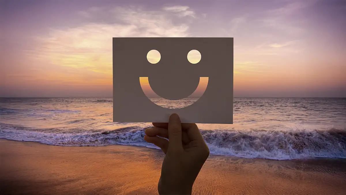 Mão segurando um papel recortado em formato smiley em uma linda praia